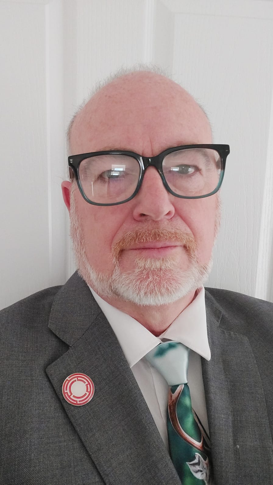 Portrait of Gavin Wright in glasses, a grey suit and a green patterned tie